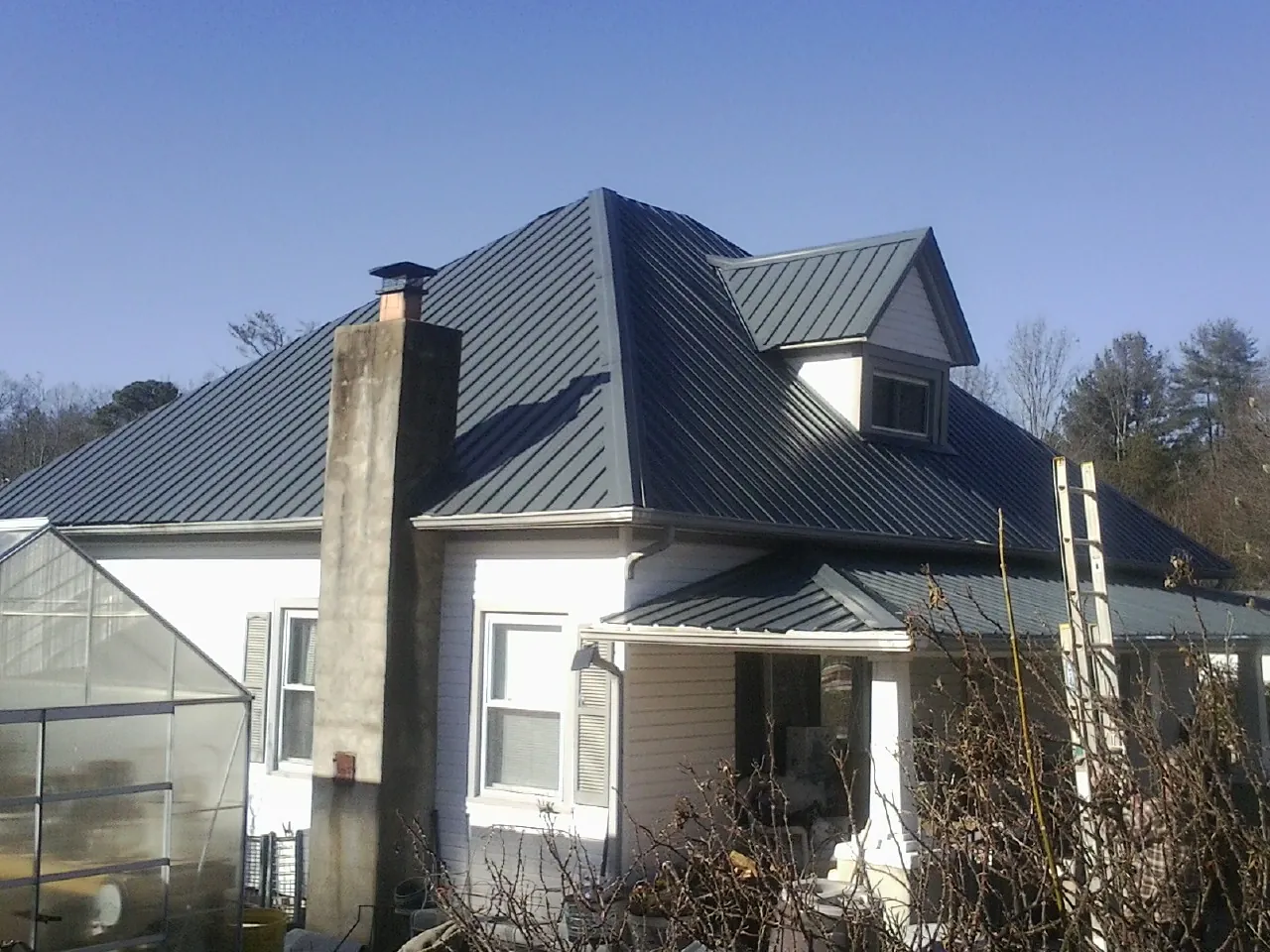 Dark blue standing seam metal roof on a white farmhouse with dormer — Slate & Tile Roof Repair by Roofing Brothers in Smicksburg