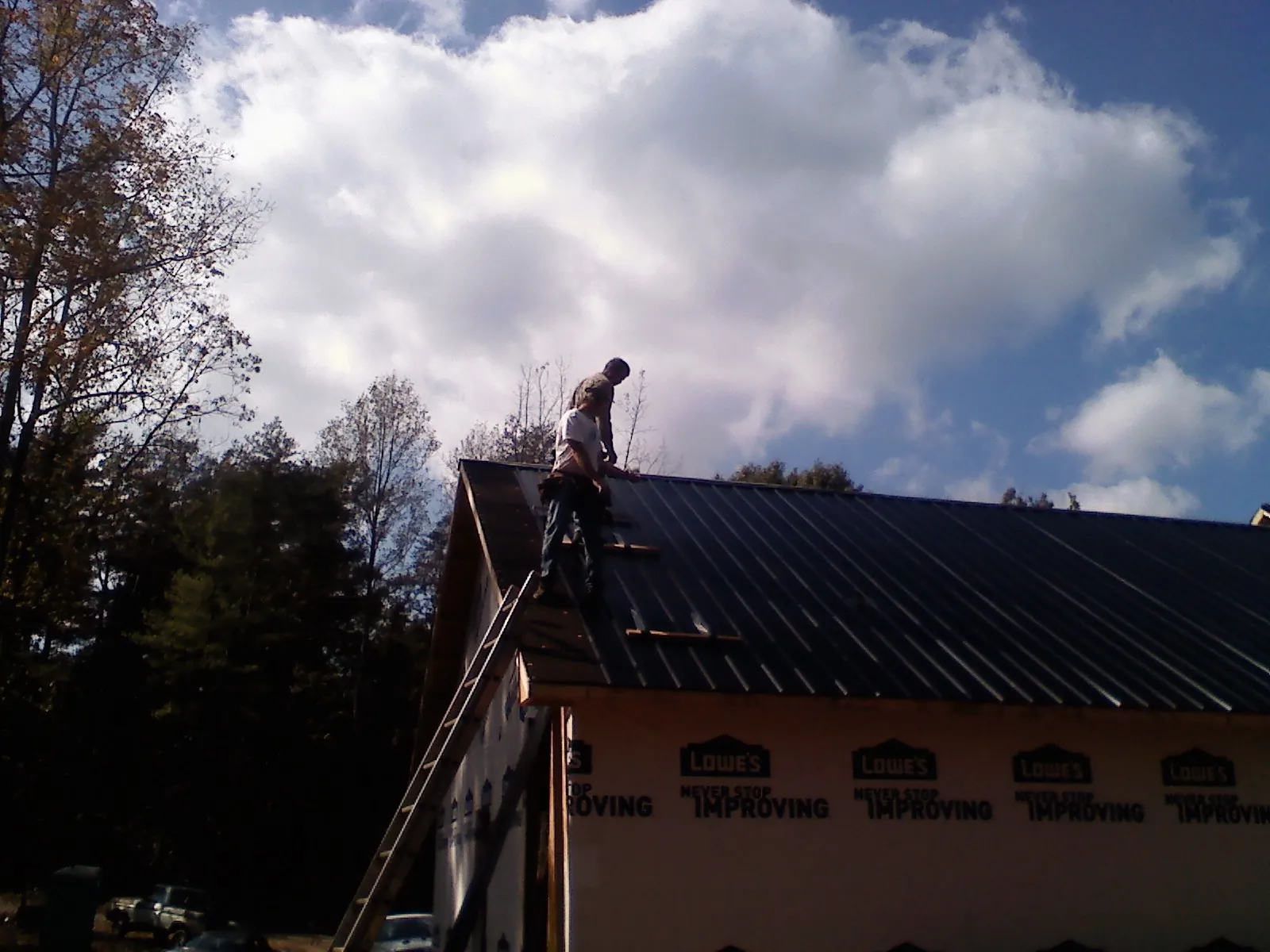 Roofer fastening dark metal panels high against a cloudy sky, from a Roof Inspection job in Smicksburg