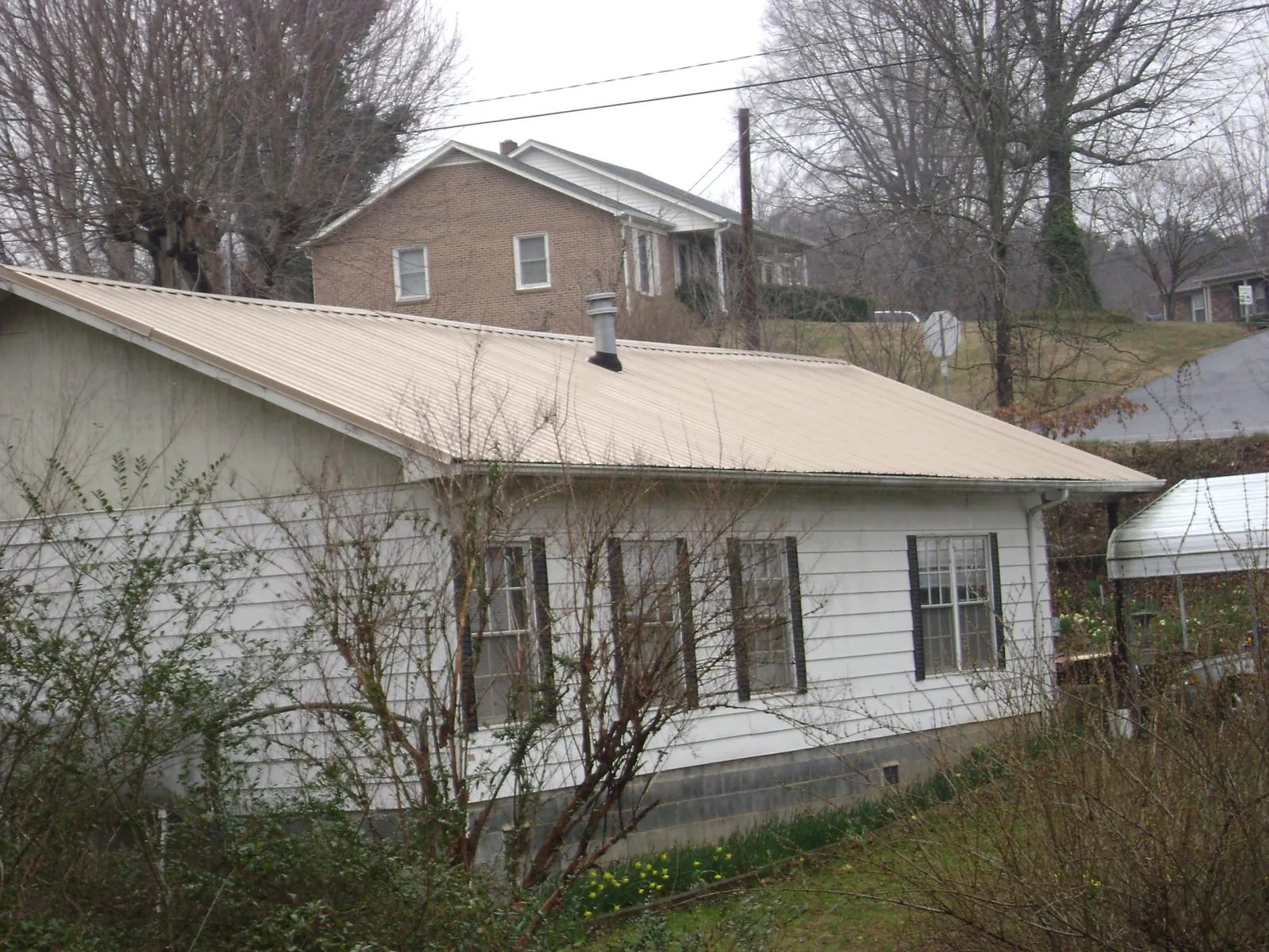 Tan metal roof on a white sided house set into a hillside — Commercial Roofing by Roofing Brothers in Smicksburg