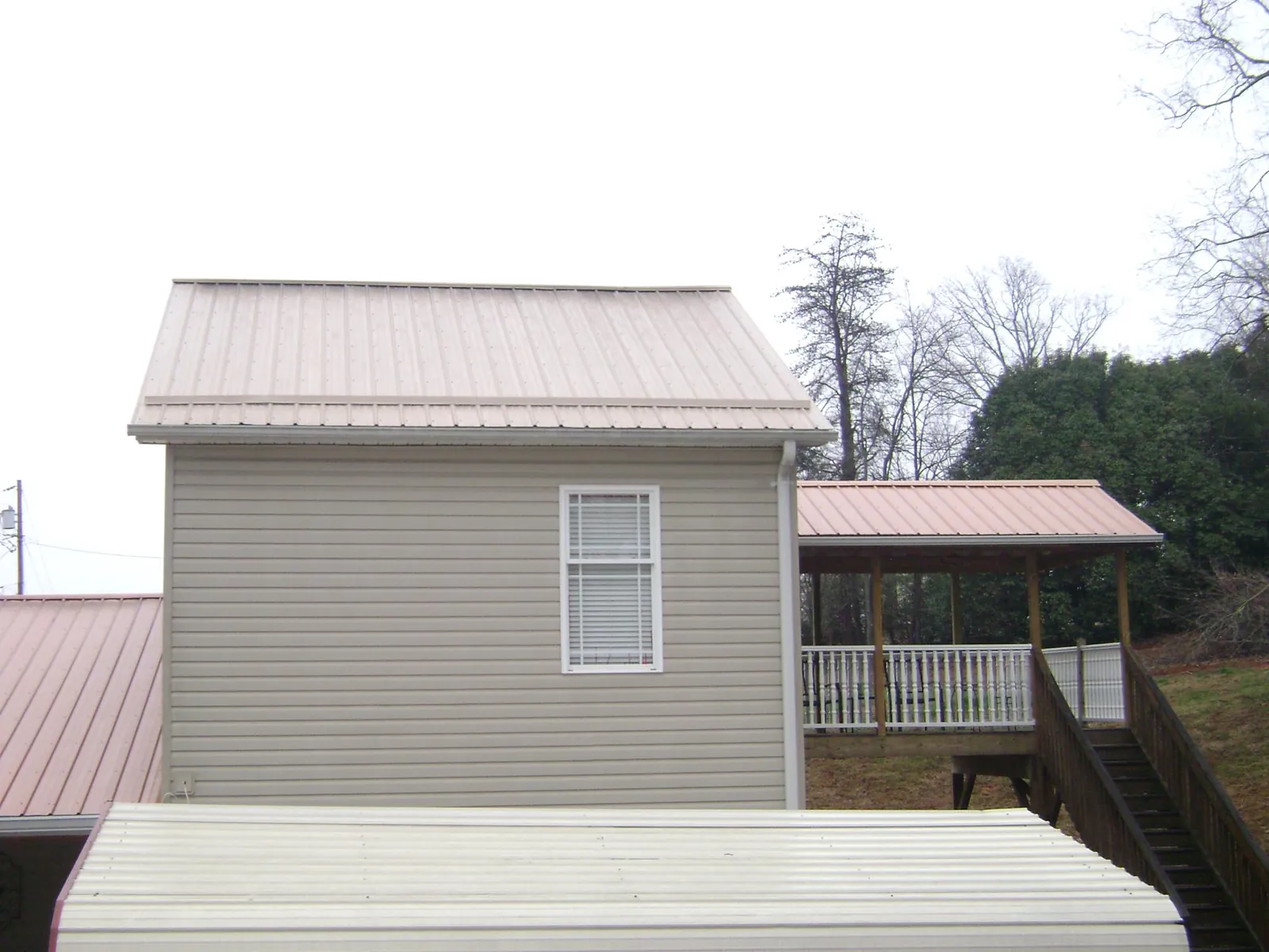Tan metal roofs on a two story addition and attached porch, from a Roof Replacement job in Smicksburg